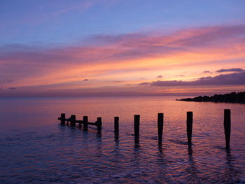 Silhouette wooden posts in sea against sky at sunset