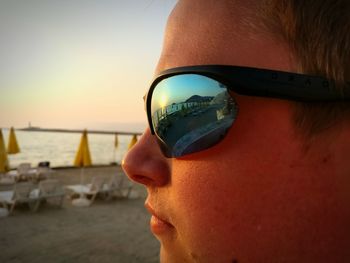 Close-up of woman wearing sunglasses against sky at sunset