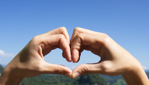 Low angle view of hands holding heart shape against blue sky