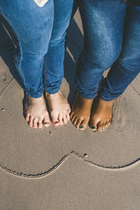 Low section of women standing in heart shape on wet sand