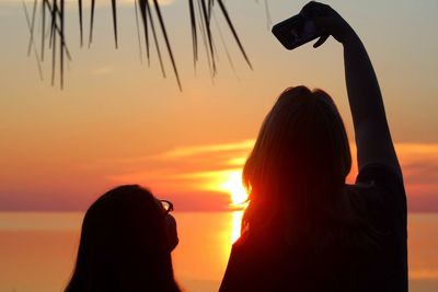 Rear view of mother and daughter taking selfie at beach during sunset