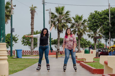 Portrait of happy friends skateboarding on footpath in park