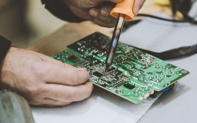 Cropped hands of engineer repairing mother board on table