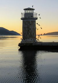 Lighthouse by sea against sky during sunset