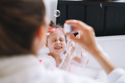 Young mother woman and little tween girl daughter having fun in the bath with foam at home