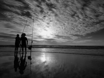 Men fishing in sea against sky during sunset