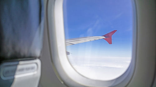 Sky scape view from clear glass window seat to the aircraft wing of the plane, traveling on clouds