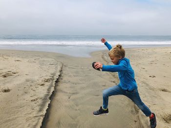 Boy jumping at beach against sky