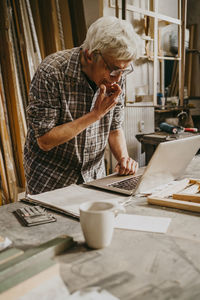 Thoughtful male carpenter with hand on chin working on laptop at repair shop