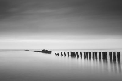 Wooden posts in sea against sky