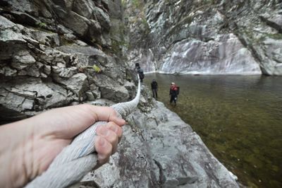 Cropped hand of person holding rope on rocks by lake