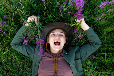 Happy young woman lying in summer grass surrounded by purple flowers. summertime wellness 