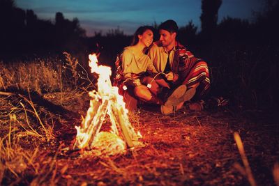 Man and woman sitting by campfire at night