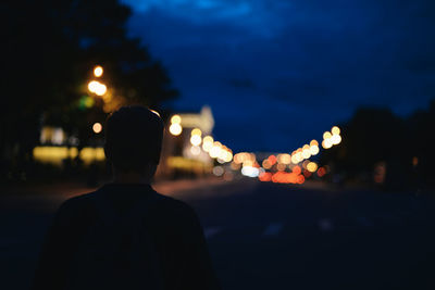 Rear view of man standing on illuminated street at night