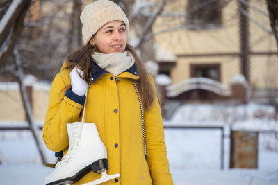 Portrait of young woman in yellow jacket with ice skates goes to rink and looking away