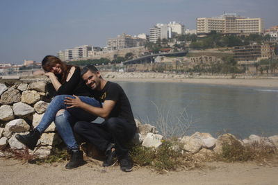 Young man sitting by river in city