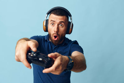 Portrait of young man holding remote control against blue background