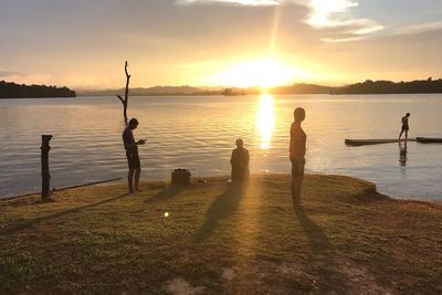 Silhouette people on lake against sky during sunset