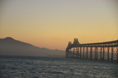 Bridge over sea against clear sky during sunset