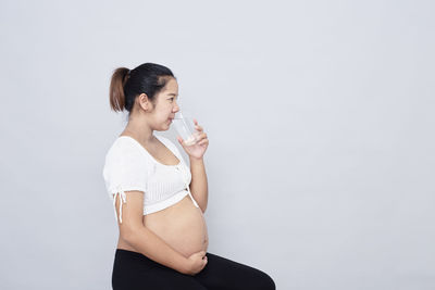 Full length of a young woman drinking glass against white background