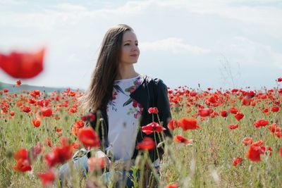 Woman standing by red poppy flowers in field