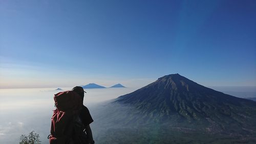 Rear view of man standing on mountain against sky