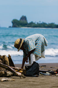 Senior woman picking drift wood at sea shore