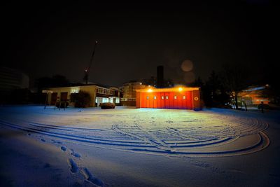 Snow covered street by buildings against sky at night