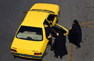High angle view of women wearing burkhas standing by yellow car on street