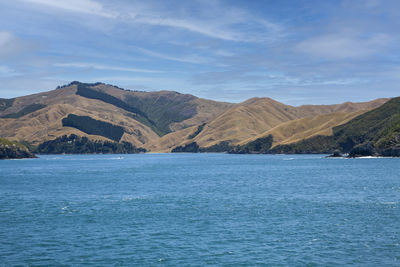 Scenic view of sea by mountain against sky