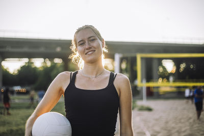 Portrait of smiling young woman holding volleyball under arm