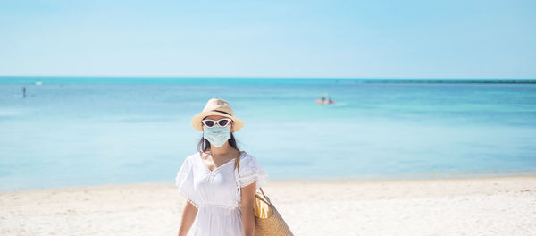 Young woman wearing mask standing on beach against sky