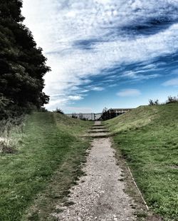 Road passing through field against cloudy sky