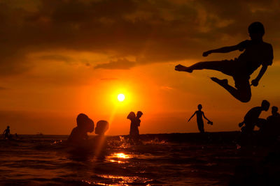 Silhouette people standing on beach against sky during sunset