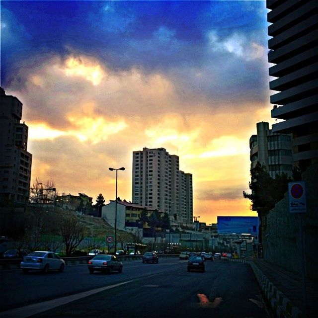 building exterior, architecture, sunset, built structure, car, city, transportation, land vehicle, sky, mode of transport, cloud - sky, street, orange color, skyscraper, city life, building, road, tall - high, traffic, cloud