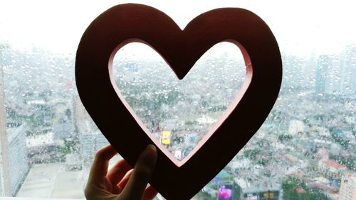 Close-up of hand holding heart shape against window