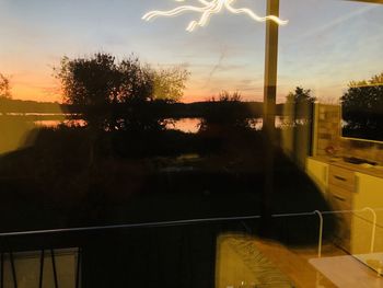 Silhouette trees against sky seen through glass window during sunset