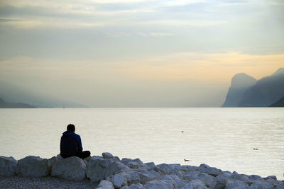 Rear view of man sitting on rock against sea