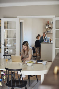 Female freelancer working on laptop while sitting at table in living room