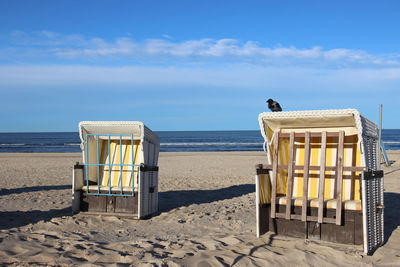 Hooded chairs on beach against sky