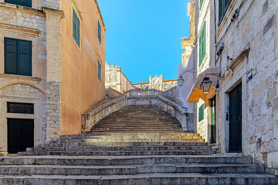 Low angle view of steps amidst buildings against blue sky