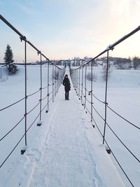 Portrait of young woman standing on snow covered footbridge against sky