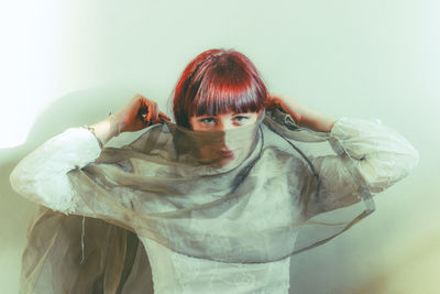 Portrait of young woman wearing hijab while standing against white background