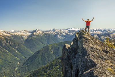 Hiker raises hands in celebration after reaching a mountain summit.