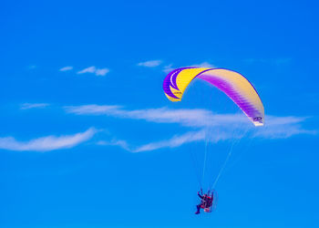 Low angle view of person paragliding against blue sky