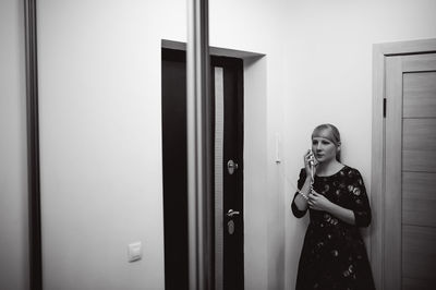 Young woman using phone while standing on door