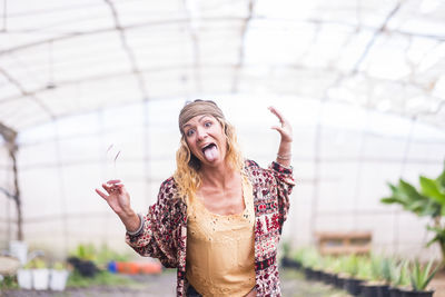 Portrait of woman making face while standing at greenhouse