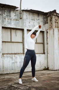Full length of young woman with arms raised exercising against wall