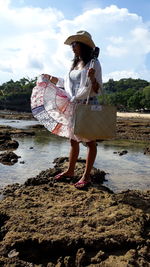 Woman standing on rock at shore against sky