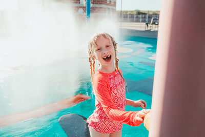 Funny girl playing on splash pad playground outdoor on summer day. seasonal water activity for kids.